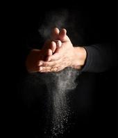 man claps his hands and scatters to the side a white substance on a black background photo