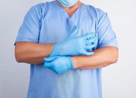 médico masculino con uniforme azul se pone en las manos guantes blancos de látex estériles antes de la cirugía foto