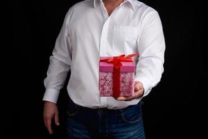 adult man in a white shirt holds a pink gift cardboard box with a bow photo