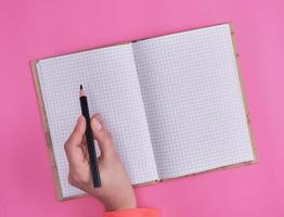 open notebook in a cell and a female hand holding a black wooden pencil photo