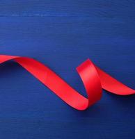 red silk thin ribbon twisted on a blue wooden background photo