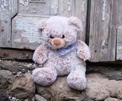 little teddy bear sits on the doorstep near an old door with cracked paint photo