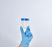 hand in a blue sterile glove holds a plastic container for collecting analyzes photo