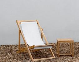 Beach chair on Pebble with White concrete wall background, Hammock chair with wooden table on white paint Cement backdrop,Vertical banner with copy space for text for Spring,Summer holidays concept photo