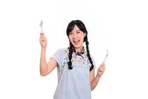 retrato de una hermosa joven asiática sonriendo con un vestido de mezclilla con cuchara y tenedor sobre fondo blanco foto