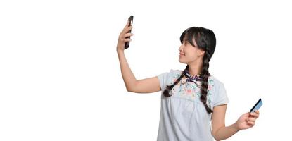 Portrait of beautiful happy young asian woman in denim dress holding credit card and smartphone on white background. studio shot photo