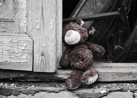 little teddy bear sits on the doorstep near an old door with cracked paint photo