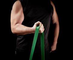 athlete with a muscular body in black clothes is doing physical exercises with green rubber photo