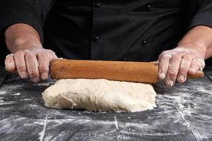 chef in a black tunic rolls a dough for a round pizza photo