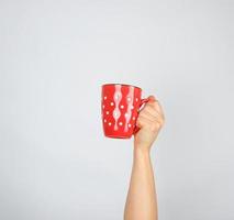 red ceramic cup in a female hand on a white background photo