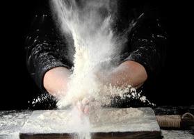 chef in black uniform sprinkles white wheat flour in different directions photo