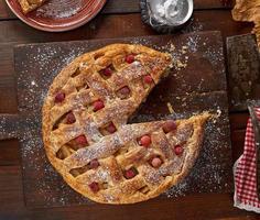 round apple pie on a rectangular old brown cutting board sprinkled with powdered sugar photo