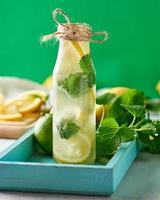 bebida fría con limones, hojas de menta, lima en una botella de vidrio foto