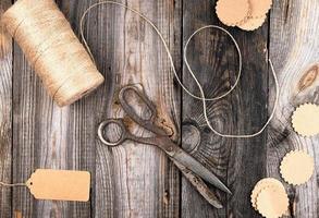 bobina de cuerda marrón, etiquetas de papel y tijeras viejas sobre un fondo de madera gris foto