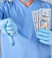 médico con uniforme azul y guantes de látex se queda con una mano mucho dinero foto