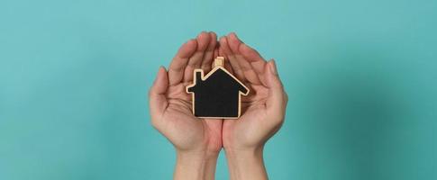 Small wood house in hands represent concepts such as home care family love real estate housing shelter insurance and mortgage. Hands holding small model house isolated on blue green studio background. photo
