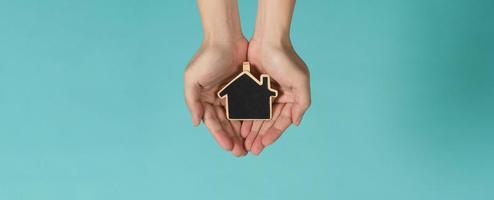 Small wood house in hands represent concepts such as home care family love real estate housing shelter insurance and mortgage. Hands holding small model house isolated on blue green studio background. photo