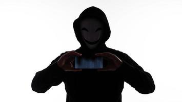 Hacker Anonymous and face mask with smartphone in hand. Man in black hood shirt holding and using mobile phone on white background. Represent cyber crime data hacking or stealing personal data concept photo