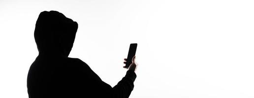 Hacker Anonymous and face mask with smartphone in hand. Man in black hood shirt holding and using mobile phone on white background. Represent cyber crime data hacking or stealing personal data concept photo