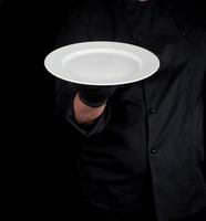 cook holds in his hand a round empty white plate photo