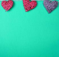 three wicker hearts hang on a rope, green background photo