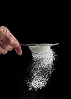 Female hand holds a metal strainer with powdered sugar. Particles fly in different directions photo