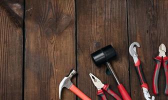 un conjunto de herramientas de construcción sobre un fondo de madera marrón, vista superior. martillo, alicates, llave ajustable foto