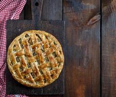 Baked whole round apple pie on a rectangular old brown board photo