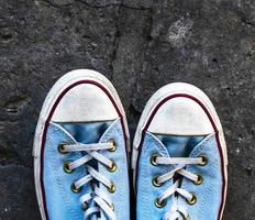 pair of old worn blue textile sneakers on gray asphalt photo