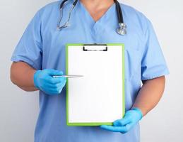 médico con uniforme azul y guantes de látex sostiene un soporte verde para hojas de papel foto