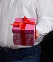 adult man in a white shirt holds a pink gift cardboard box with a bow photo