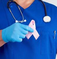 doctor in blue uniform and sterile latex gloves holds a pink ribbon photo