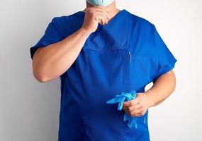 doctor in blue uniform holds sterile latex gloves and puts on a mask photo