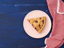 triangular slice of baked cherry pie on a pink round plate photo