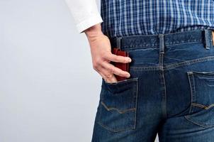 man in a blue plaid shirt and jeans puts a leather wallet in his back pocket photo