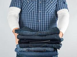 man in jeans and blue plaid shirt holding a pile of jeans photo