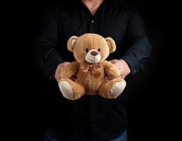 hombre adulto con una camisa negra sostiene un oso de peluche marrón foto