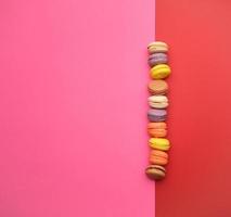 round multi-colored baked macarons with cream lie in a line on a pink background photo