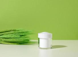 empty white jar for cosmetics on white table, green background. Packaging for cream, gel, serum, advertising and product promotion. Mock up photo