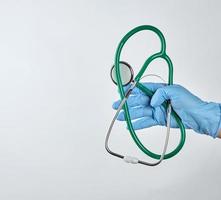 mano enguantada estéril azul sosteniendo un estetoscopio médico verde foto