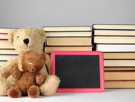 brown teddy bear and empty black board in red frame on the background of pile of books photo