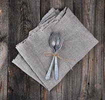 tenedor y cuchara de metal antiguo atados con una cuerda marrón en una servilleta de lino gris foto