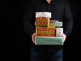 adult man in a black shirt holds in his hands a stack of paper-wrapped gifts on a black background photo