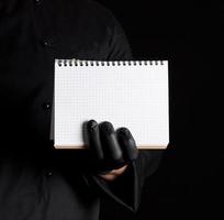 Chef in black uniform and black latex gloves holding a blank notebook photo