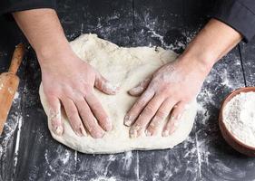 men's hands knead a round piece of dough for making pizza photo