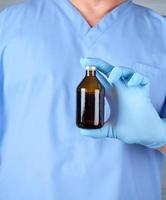 médico con uniforme azul y guantes de látex sosteniendo una botella de vidrio marrón foto