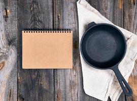 empty black round frying pan with handle and paper notebook photo