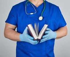 doctor en uniforme azul sostiene un libro abierto en sus manos foto