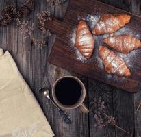 ceramic brown cup with black coffee and wooden cutting board with baked croissants photo