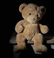 aold brown teddy bear is sitting on a wooden surface photo